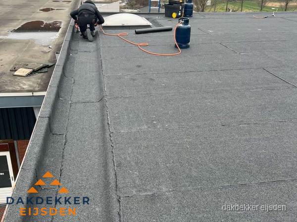Dakdekker repareert bitumen dakbedekking op groot plat dak in Eijsden